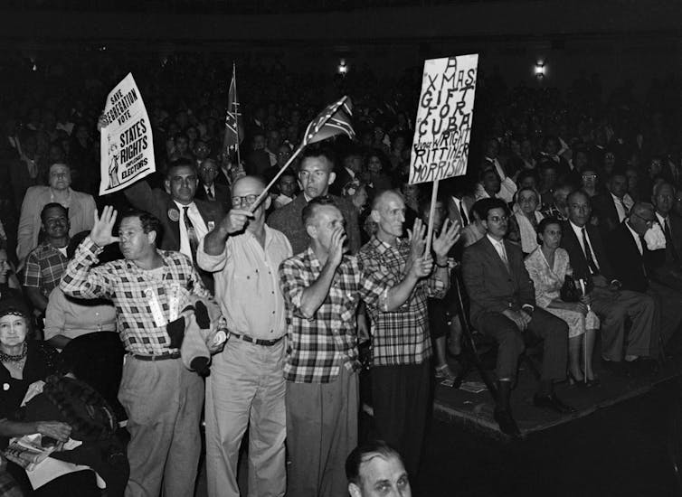 A crowd of white people wave racist placards.