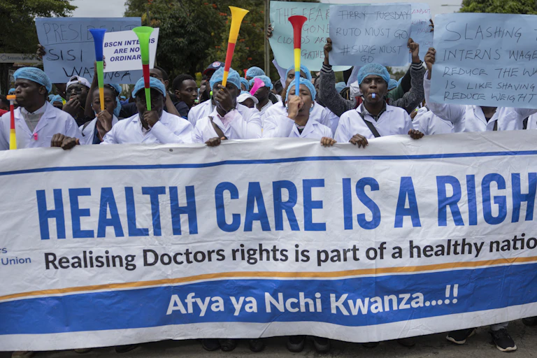 A crowd of people blowing vuvuzelas and holding up a placard written 'Healthcare is a right'