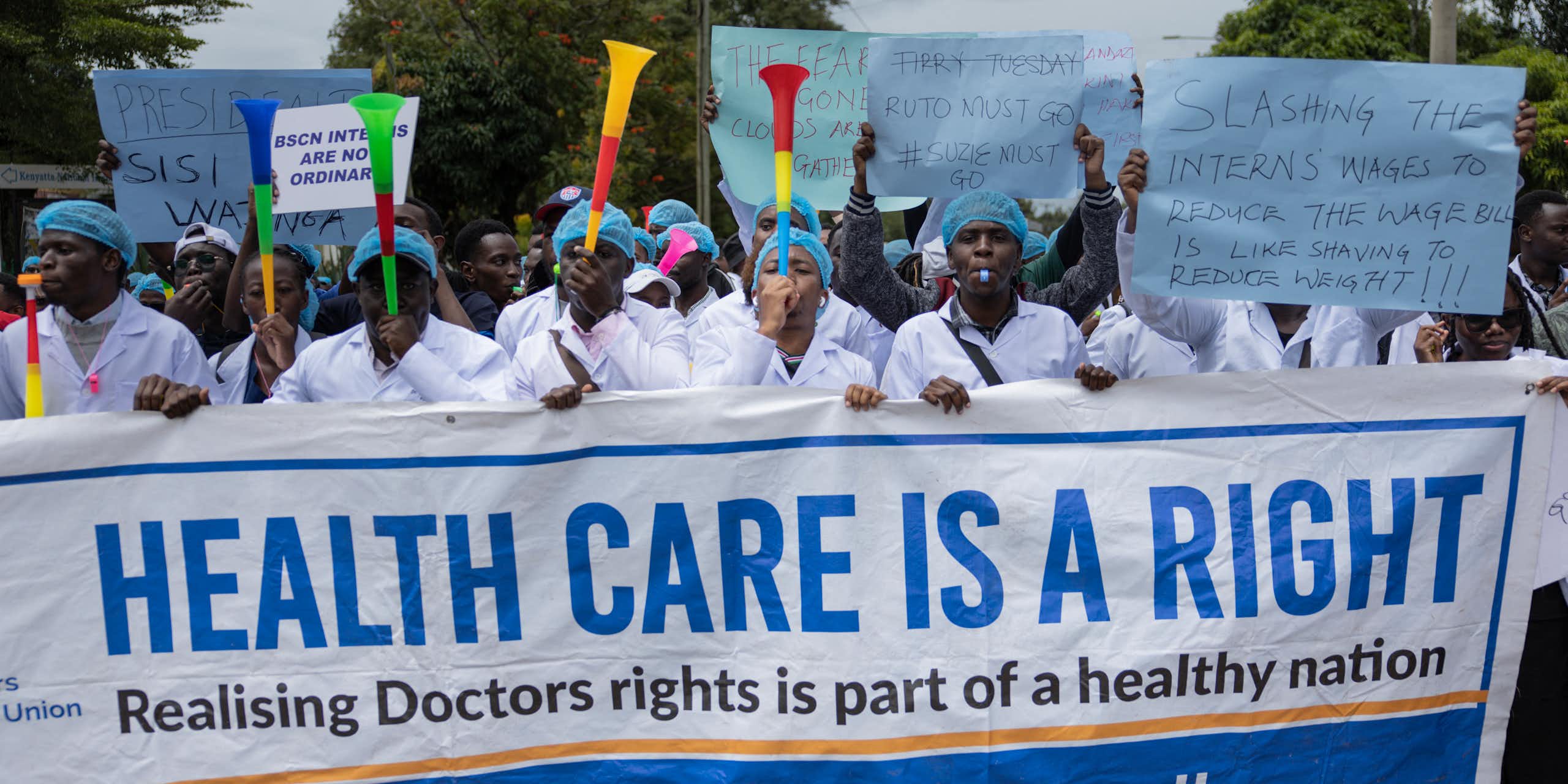 A crowd of people blowing vuvuzelas and holding up a placard written 'Healthcare is a right'