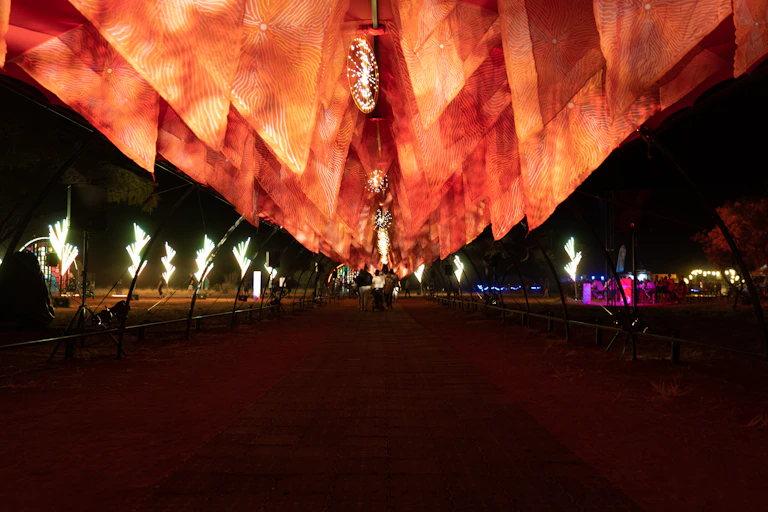 A red sand path beneath a large orange light installation with Aboriginal artworks projected onto it.