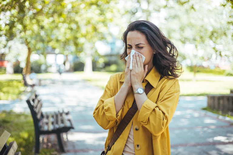 Woman in park blowing her nose with tissue or hankerchief
