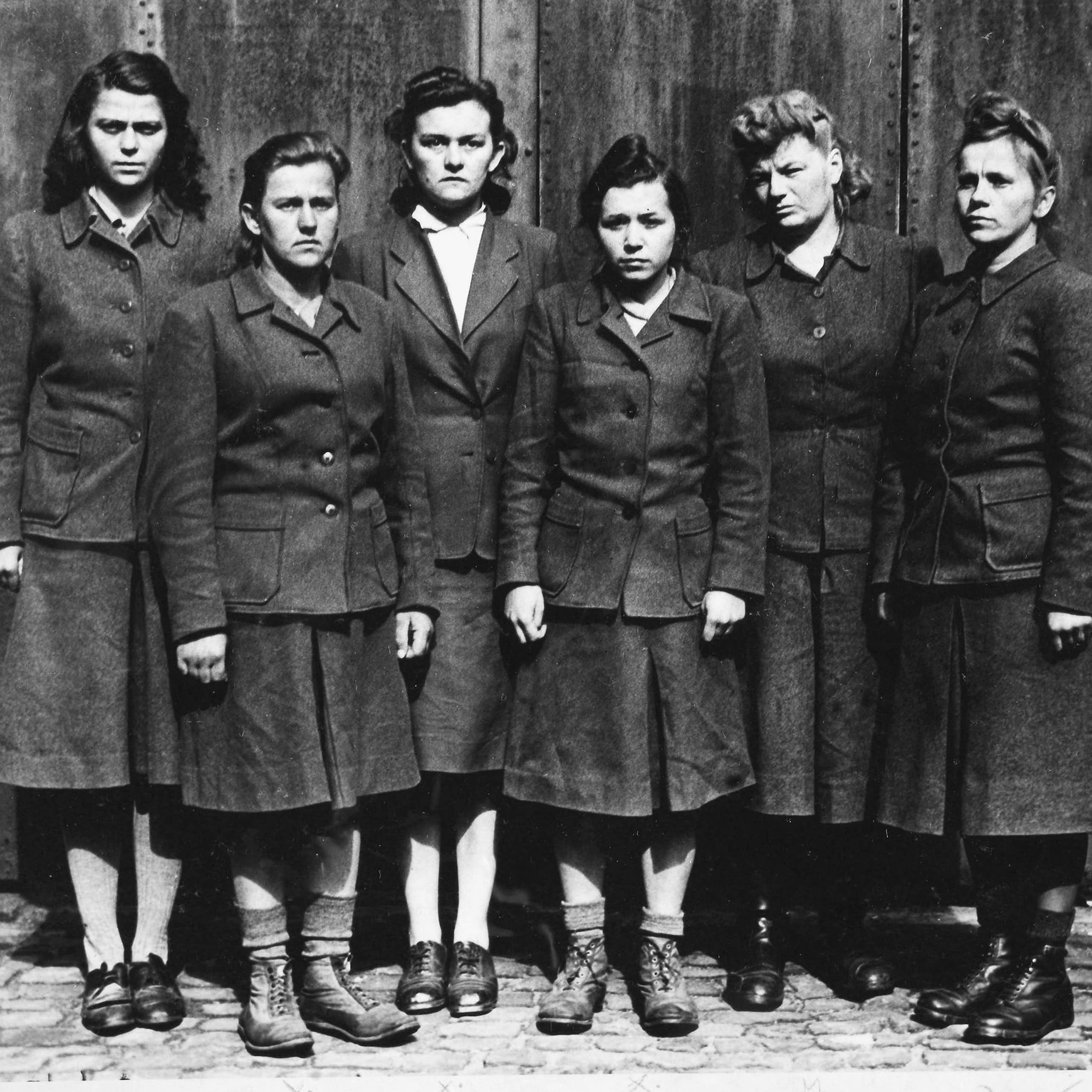 Six female SS guards from Belsen standing in a row scowling at the camera.