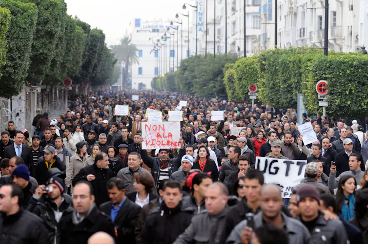 Tunisian people protesting with a sign in red reading