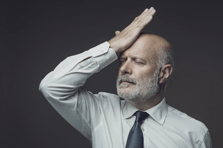 Man in shirt and tie holds hand to forehead with eyes shut