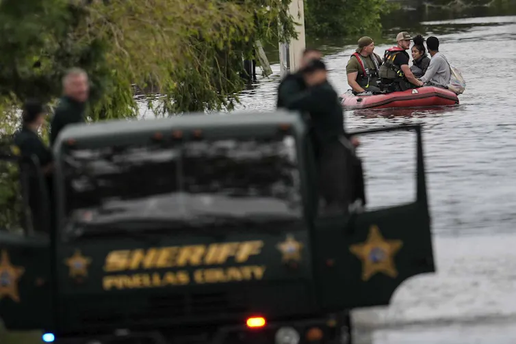 A rescue boat carries people toward a sheriff's vehicle.