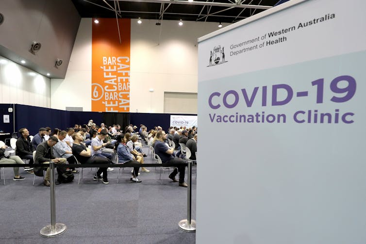 A sign reading 'COVID-19 Vaccination Clinic' with people waiting in the background.
