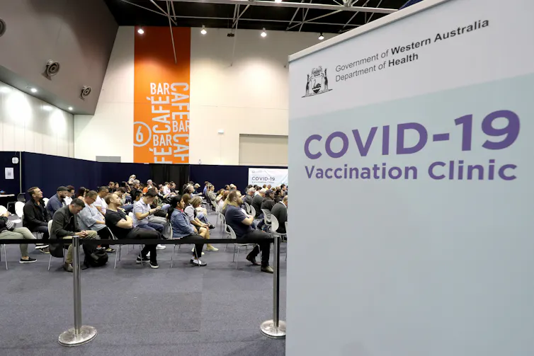 A sign reading 'COVID-19 Vaccination Clinic' with people waiting in the background.