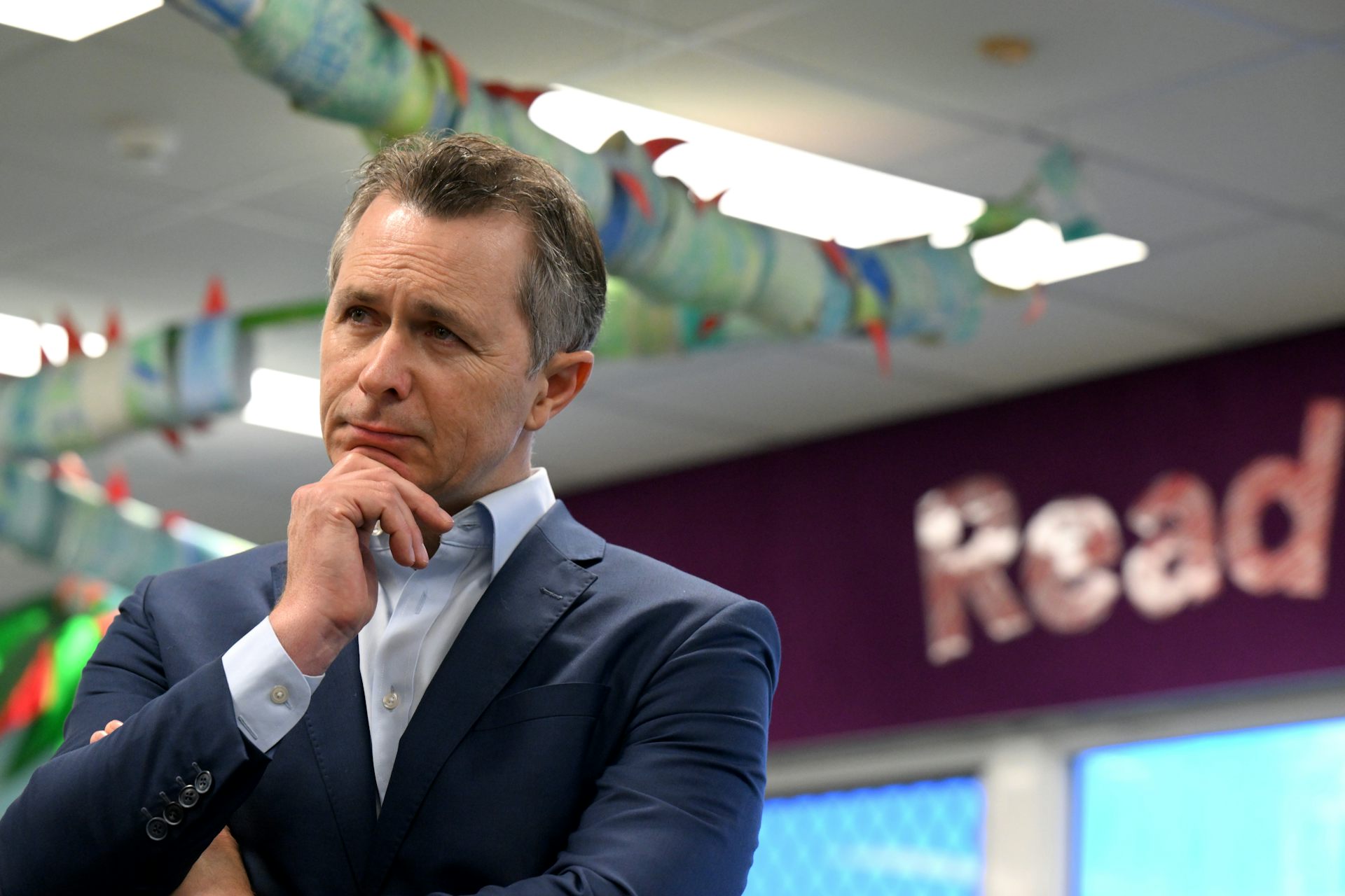 Education Minsiter Jason Clare stands in a school library in front of a sign that says 'read'.