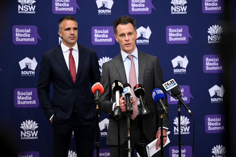 Two men in suits speaking to the media in front of microphones.