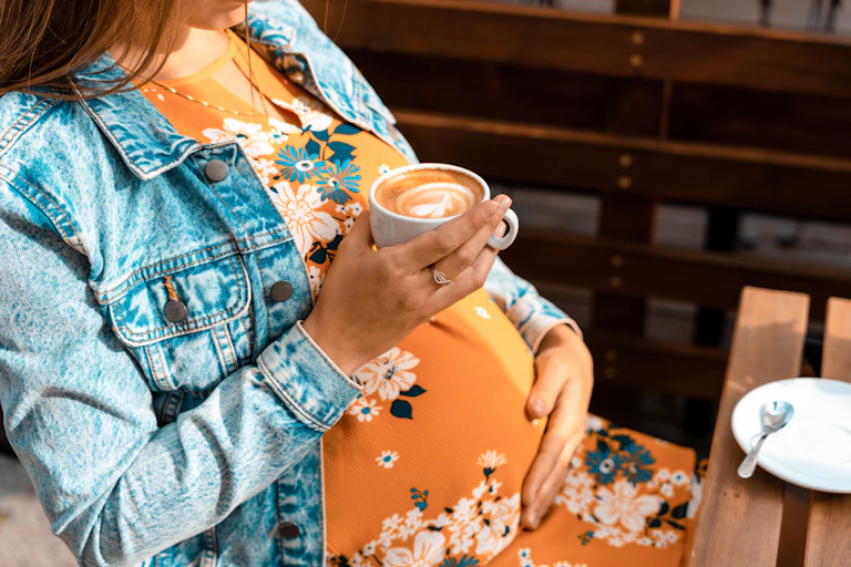A woman in yellow dress holds a flat white above her pregnant belly.