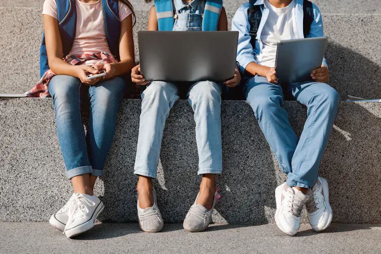 Legs of preteens seen with devices.