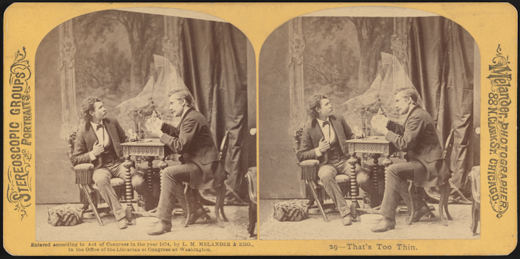 A ghost looms behind a card table, pointing an accusing hand at one of the two seated men playing there.