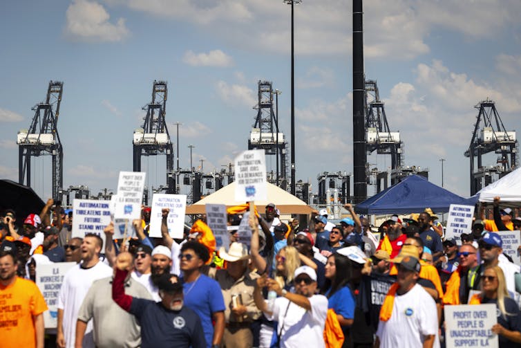 Cranes are seen in the background of a crowd of protesters holding signs