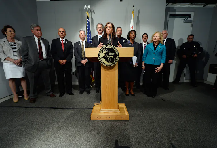 A woman speaks at a lectern with a group of people behind her.