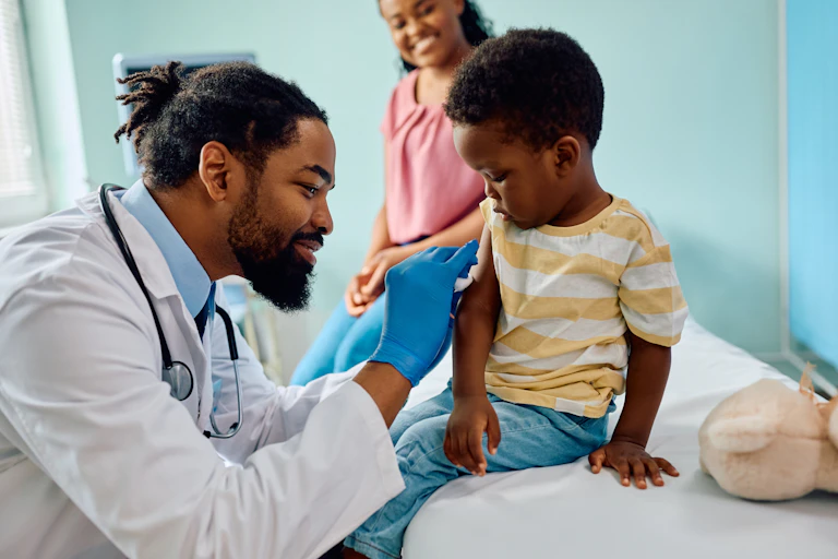 A doctor giving a little boy a shot with his mother in the background