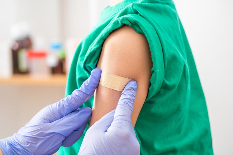Cropped image of gloved hands applying an adhesive bandage to someone's arm