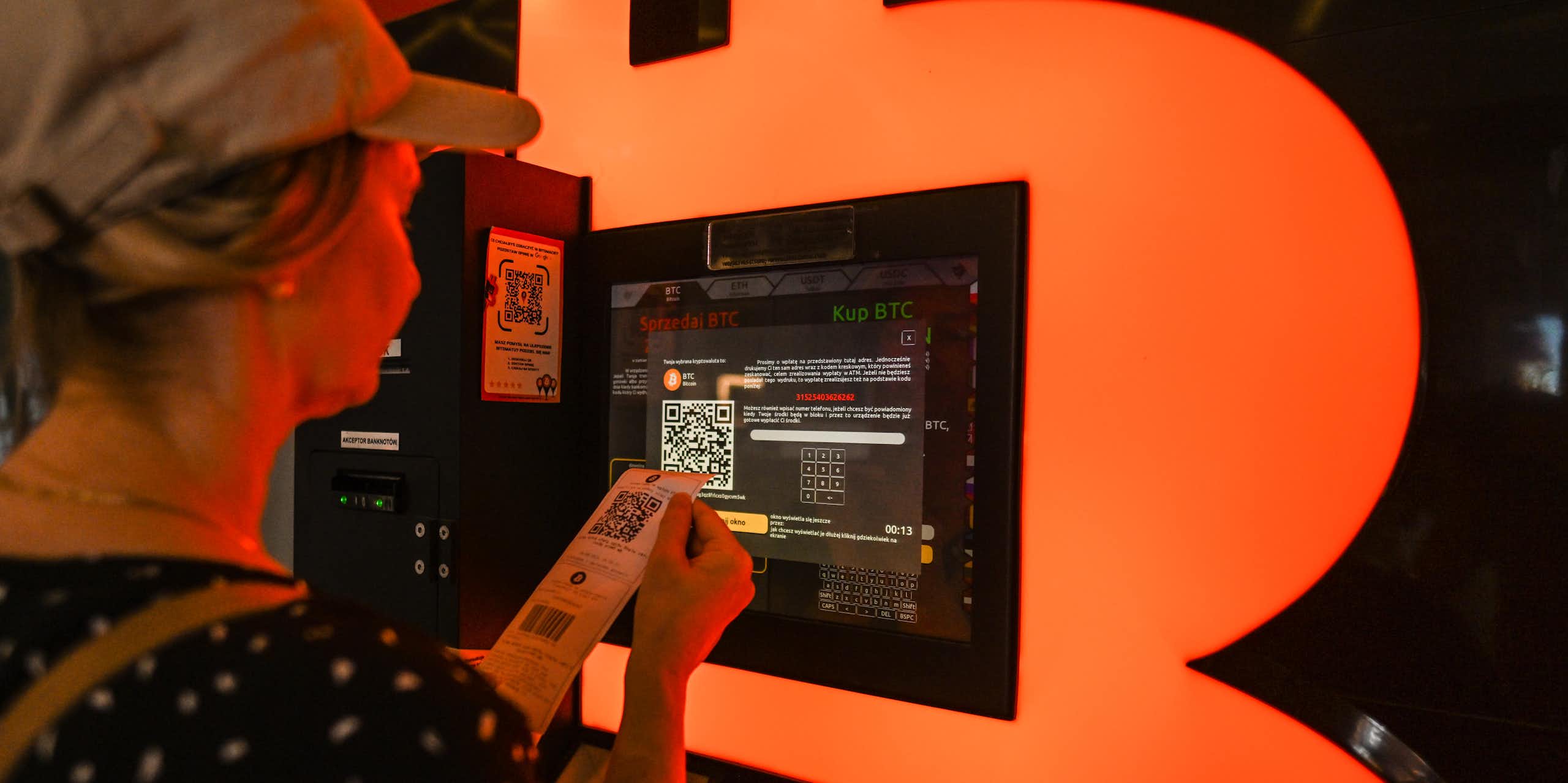 A woman looks intently at a screen while holding a narrow sheet of paper with a QR code on it.