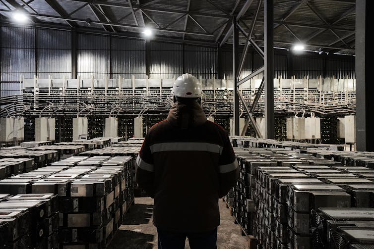 The back of a man standing in a data center filled with computer servers.