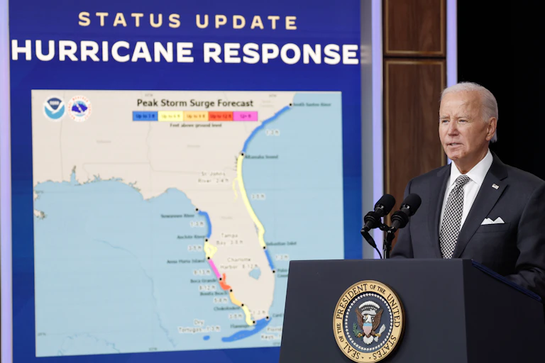 A man in a suit at a lectern next to a sign that says 'STATUS UPDATE HURRICANE RESPONSE' above a map of the state of Florida.