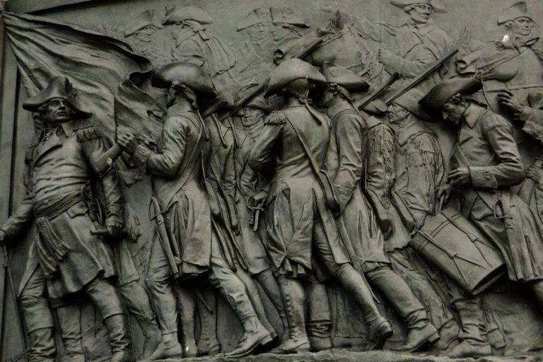 A pewter-colored relief showing a small crowd of soldiers walking.