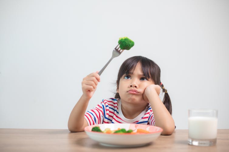 A child makes a disgruntled face while looking at a floret of broccoli on her fork