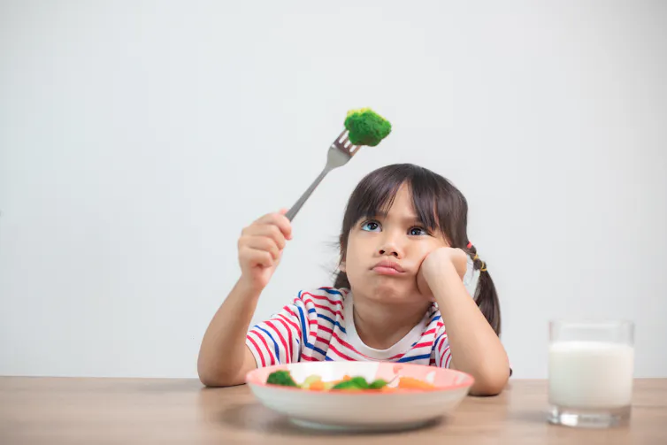 A child makes a disgruntled face while looking at a floret of broccoli on her fork