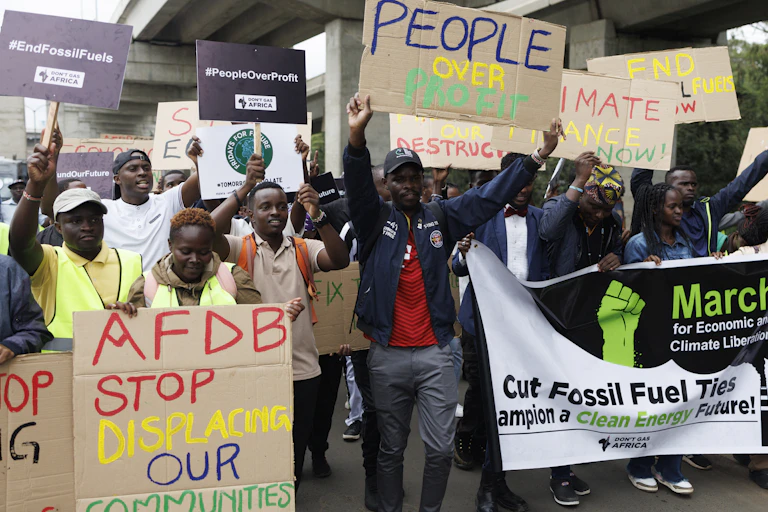 Protestors march with placards that say End Fossil Fuels, AFDB stop displacing our communities, Climate Finance Now, Cut Fossil Fuel Ties, and People over Profit