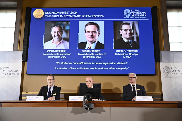 Three men in suits announcing the winners of the 2024 Nobel prize in economics.