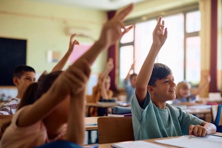 Des élèves qui lèvent la main en classe