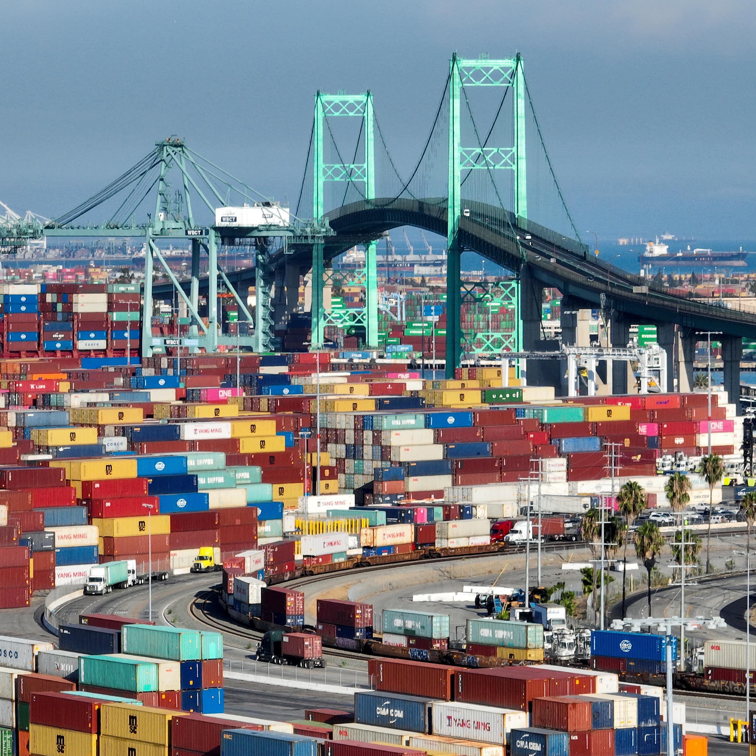 The Vincent Thomas Bridge, a 1,500-foot-long suspension bridge, is visible behind many dozen multicolored cargo containers.