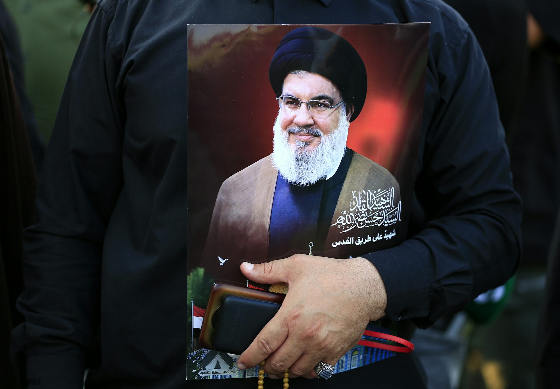 A man holding carrying an image of Hassan Nasrallah.