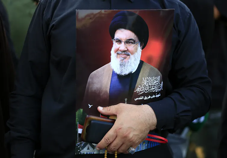 A man holding carrying an image of Hassan Nasrallah.