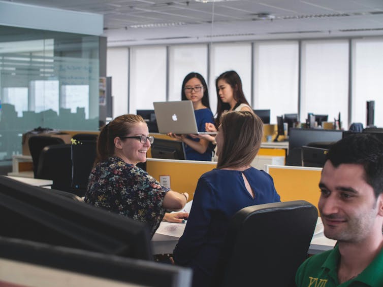 Office workers smile and talk to each other.