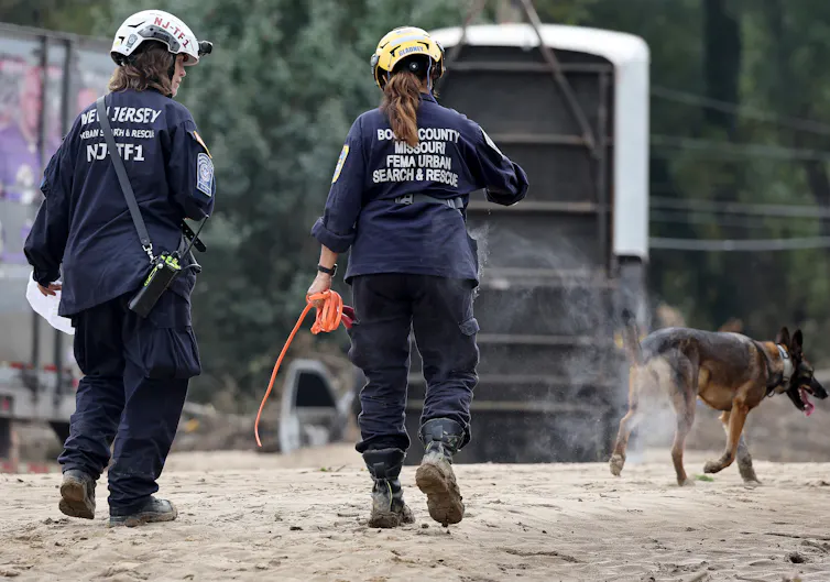 Twopeople in rugged uniforms and helmets walking along with a dog.