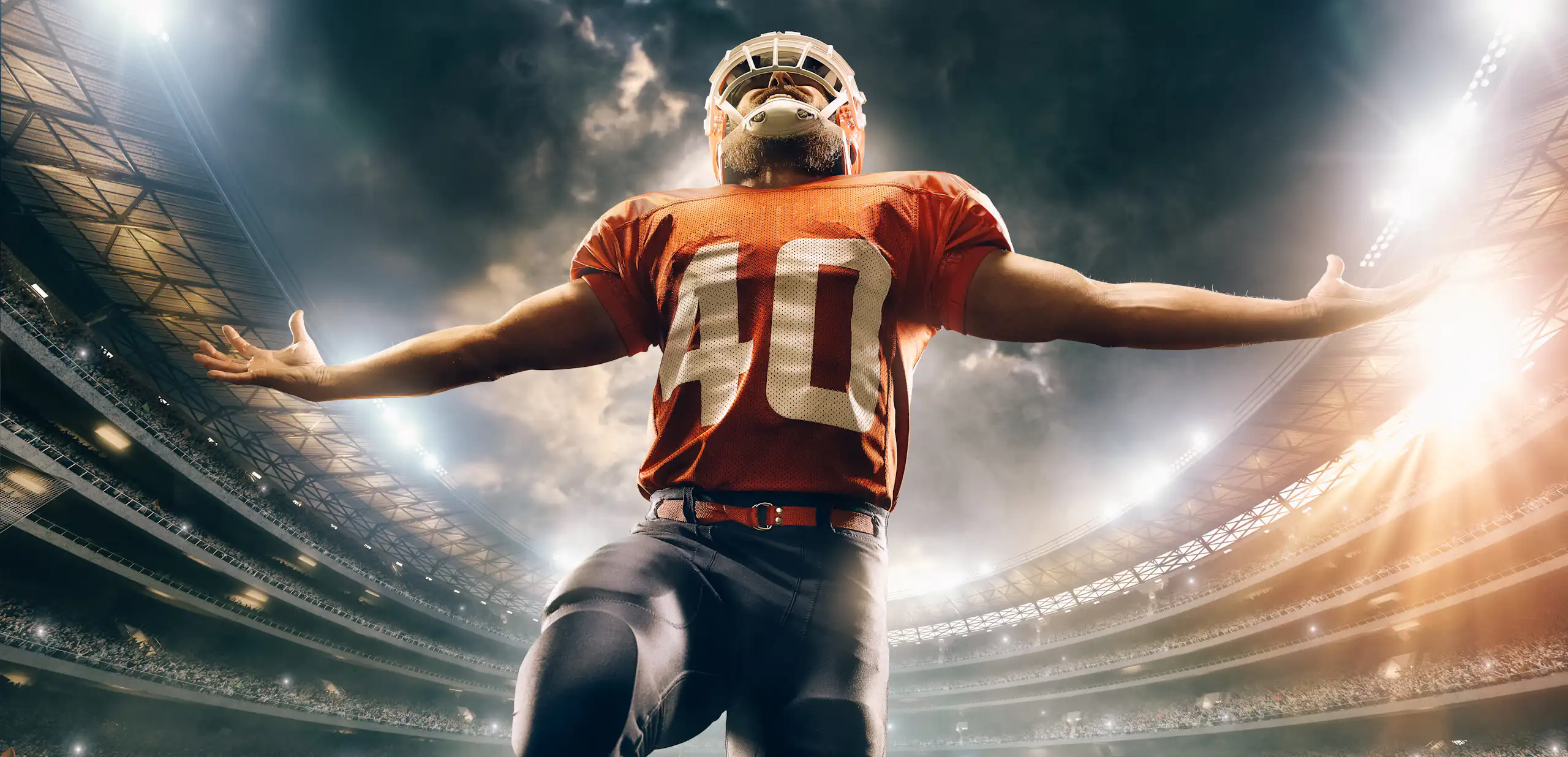 A football player extends his arms in a stadium full of people underneath the evening or night sky.
