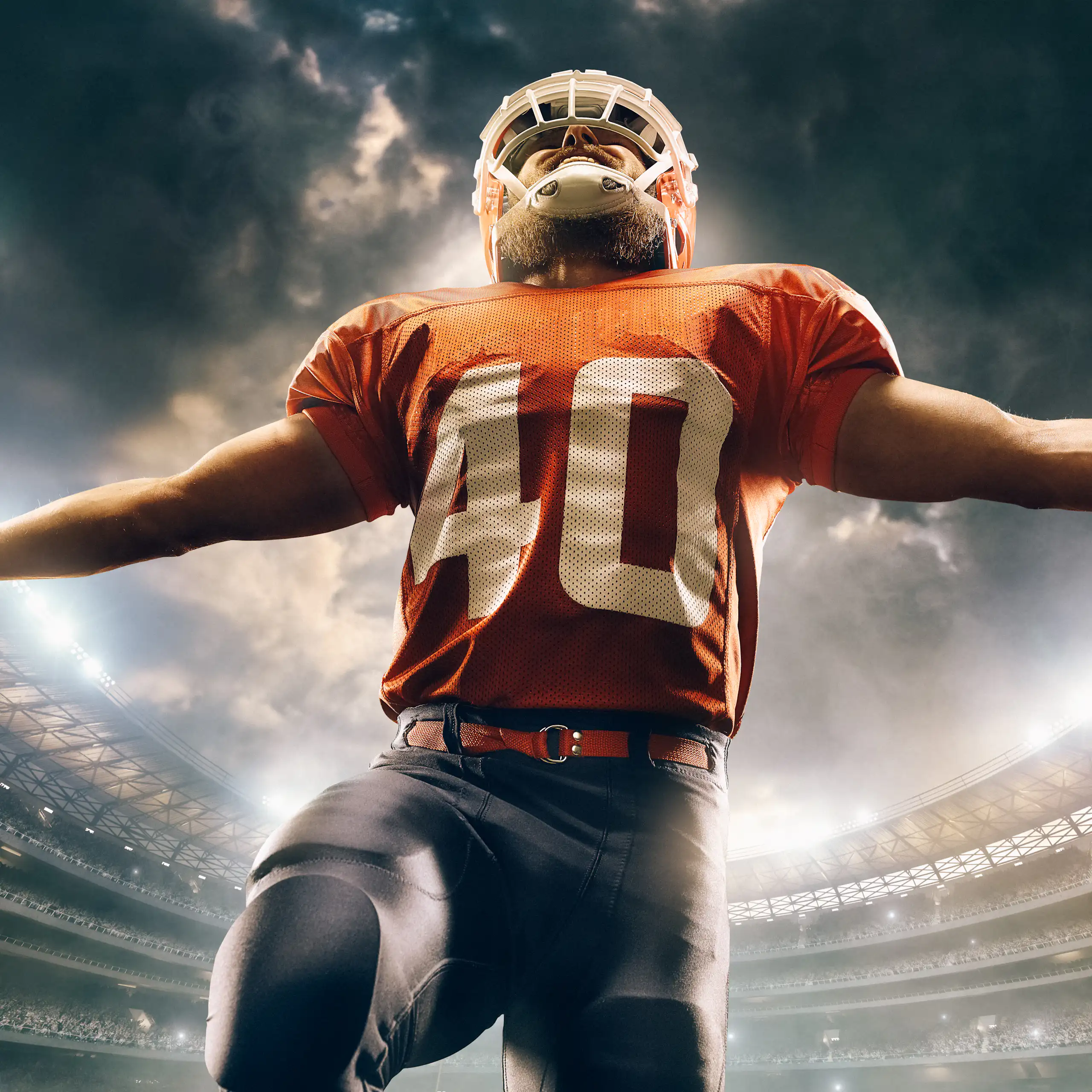 A football player extends his arms in a stadium full of people underneath the evening or night sky.