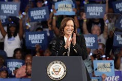 A Black woman stands behind a podium as scores of people hold up campaign signs.