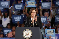 A Black woman stands behind a podium as scores of people hold up campaign signs.