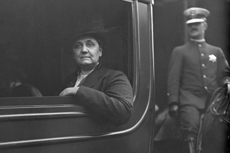 Black and white photo of a middle-aged woman sitting in a car with her arm hanging out of the window.