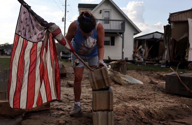 A woman wades through mud and places an American flag near a mobile home that was destroyed during a hurricane.