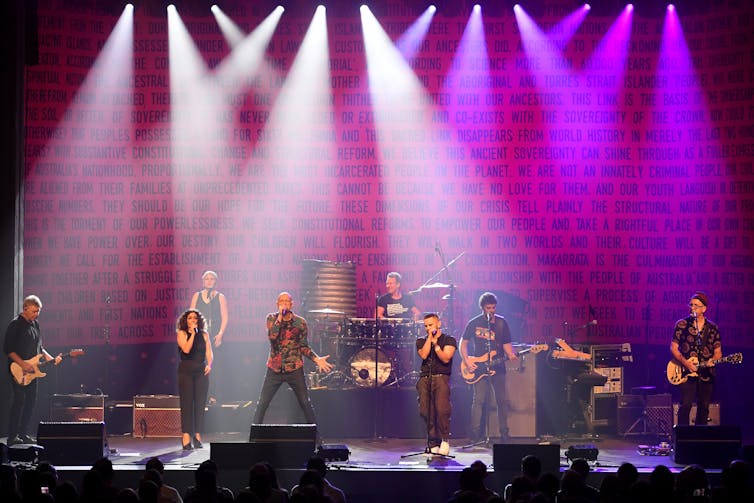 musicians performing onstage with purple stage lights