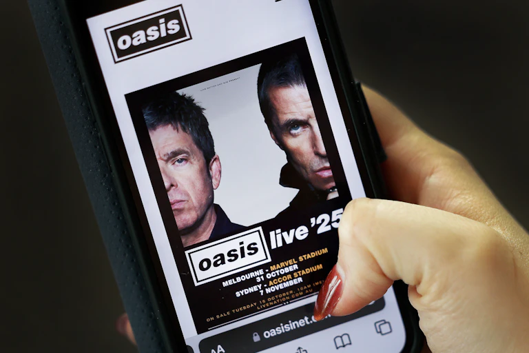 band 'oasis' tour info shown on mobile phone being held by woman's hand