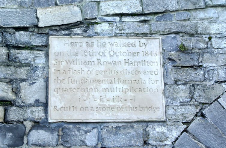 Photo of a plaque with inscription 'Here as he walked by on the 16th of October 1843 Sir William Rowan Hamilton in a flash of genius discovered the fundamental formula for quaternion multiplication i²=j²=k²=ijk=-1 & cut it on a stone of this bridge.'