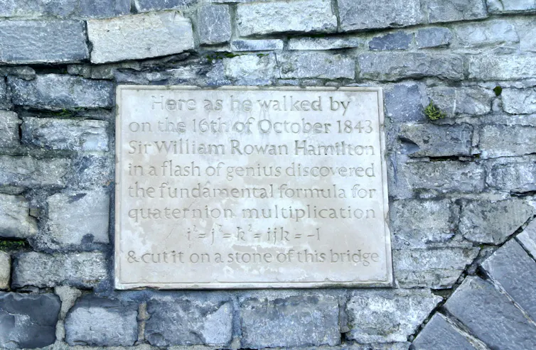 Photo of a plaque with inscription 'Here as he walked by on the 16th of October 1843 Sir William Rowan Hamilton in a flash of genius discovered the fundamental formula for quaternion multiplication i²=j²=k²=ijk=-1 & cut it on a stone of this bridge.'