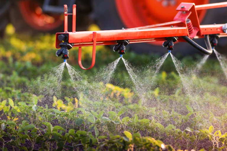 A tractor's red spray arm applying pesticide to crops.