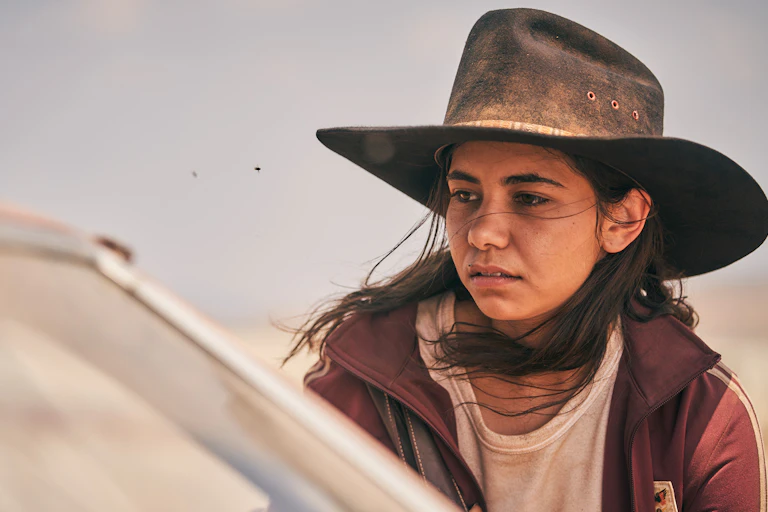 girl in large hat looks into car window in rugged outdoor setting