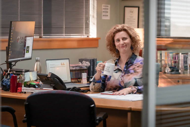 woman sits at desk holding mug