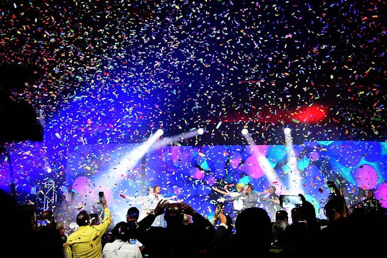 A stage bathed in lights, a shower of confetti and people with raised arms.