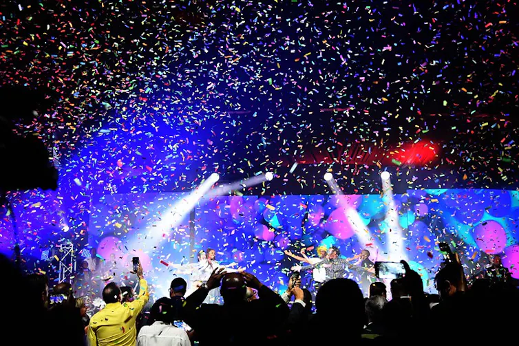 A stage bathed in lights, a shower of confetti and people with raised arms.