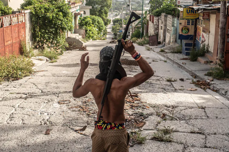 An armed Haitian man looking down a derelict street.